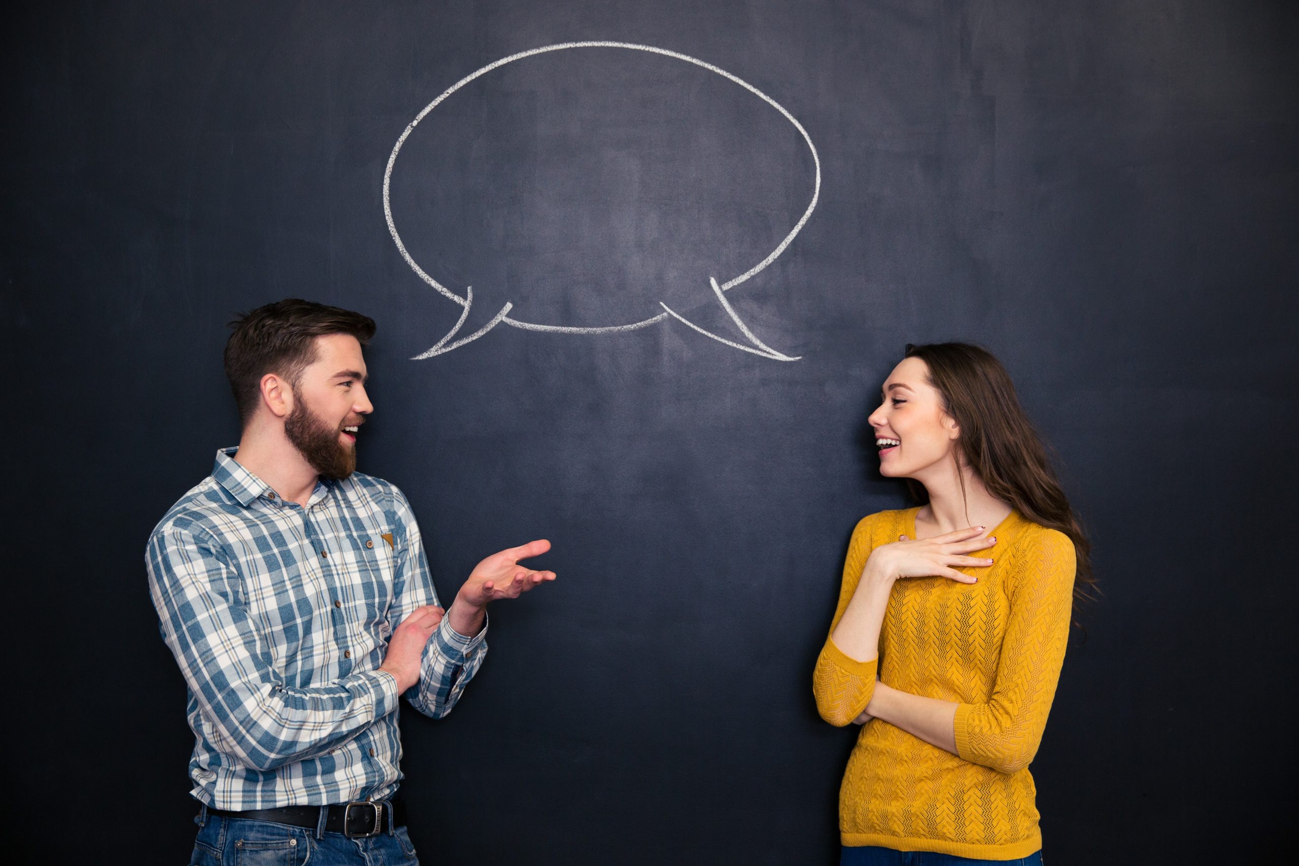 Happy young couple talking over chalkboard background with drawn empty dialogue